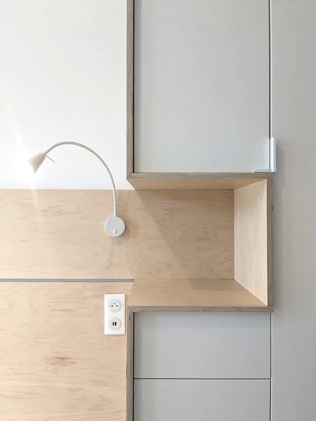 Détail d’un agencement en bois clair, avec une niche et un éclairage de lecture.